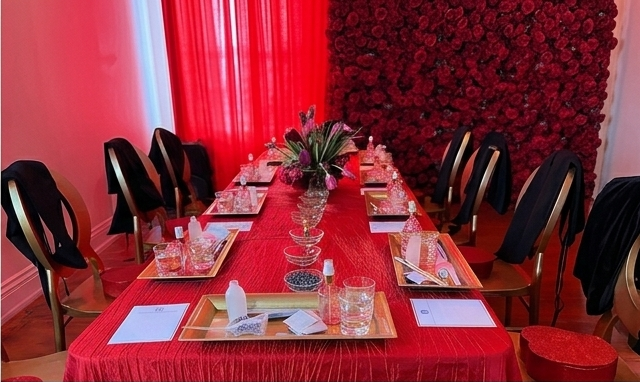 Red linen banquet table styled with a rose wall backdrop and fragrance trays